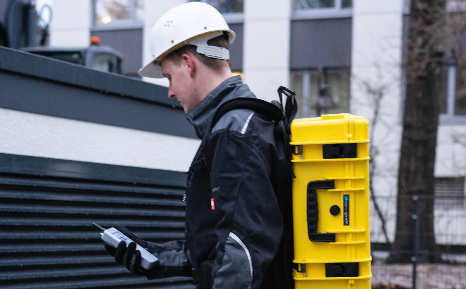ENQT Mitarbeiter mit gelben Messkoffer und Netztester LTE vorm Gebäude stehend